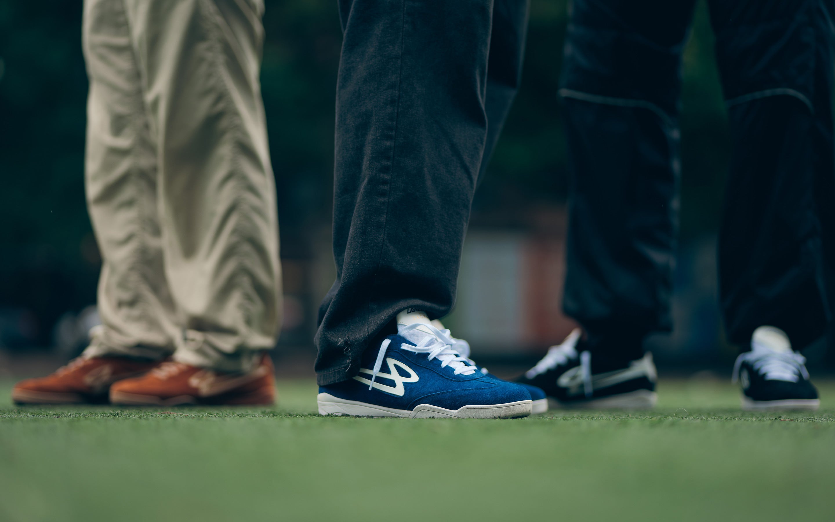 Close-up of three people wearing Lanzera Jackal shoes in navy, black, and caramello on turf.