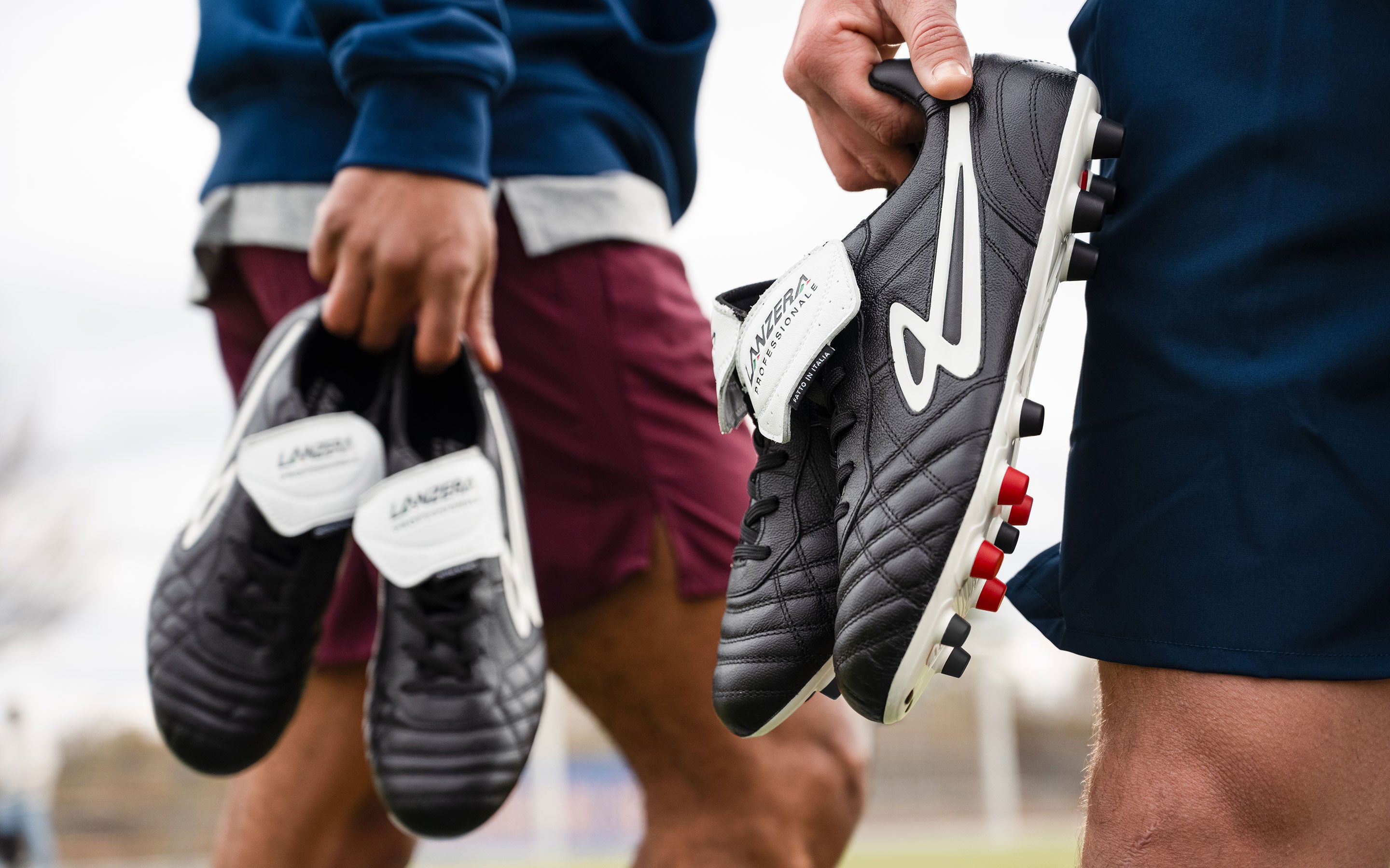 Two players holding Lanzera Professionale black K-leather soccer cleats.